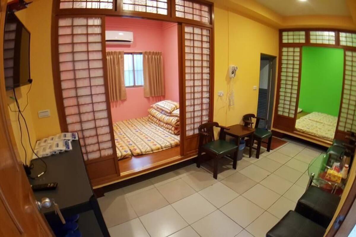 A room with a bed, a desk, a chair, a small table, and a green screen.