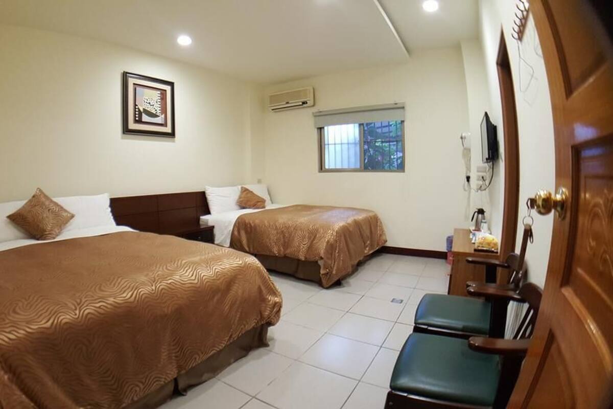 A hotel room with two beds, a small desk, a chair, a window, and a door.