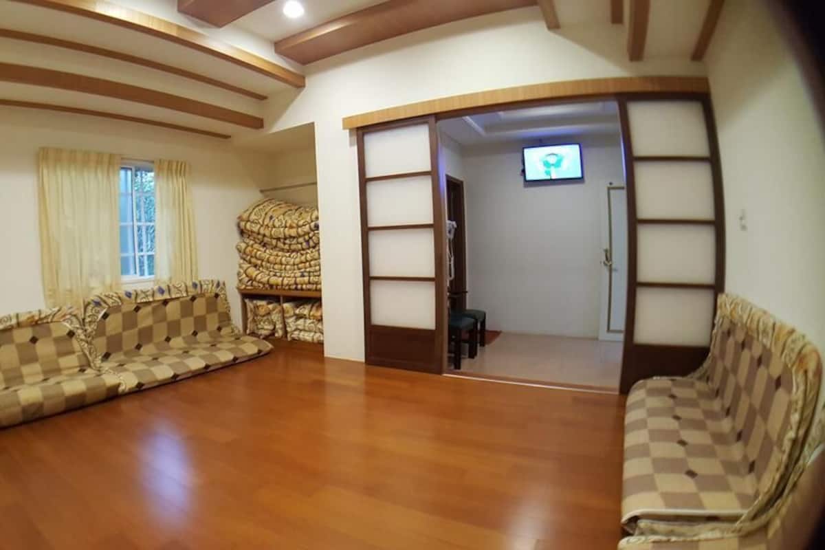 A spacious living room with a checkered sofa set, a wooden floor, and a television in the background.