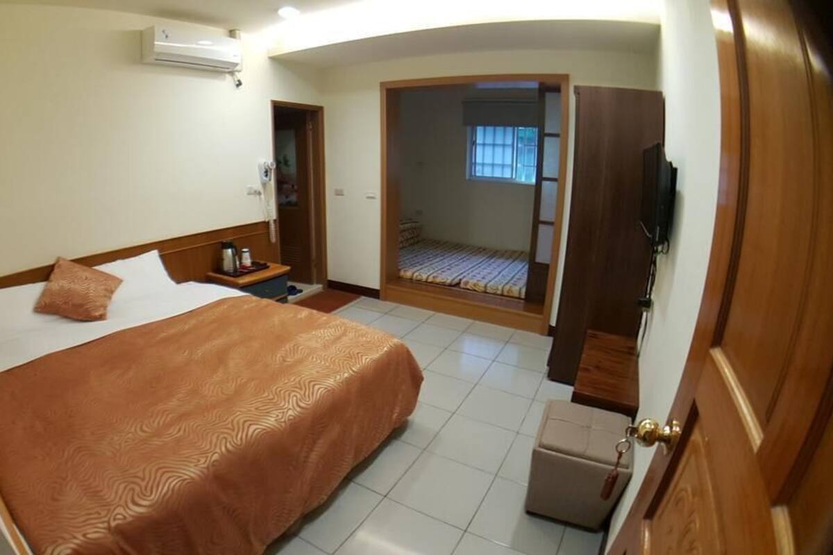 A hotel room with a bed, bedside table, and a small desk. There is a door leading to a balcony.