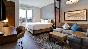 A modern hotel room with a large bed, a sofa, a desk, and a television. - Hyatt Place Prince George (Prince George)
