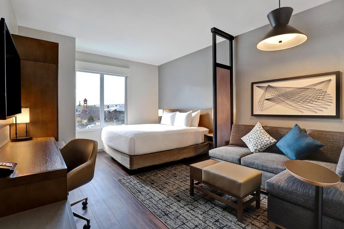 A modern hotel room with a large bed, a sofa, a desk, and a television.