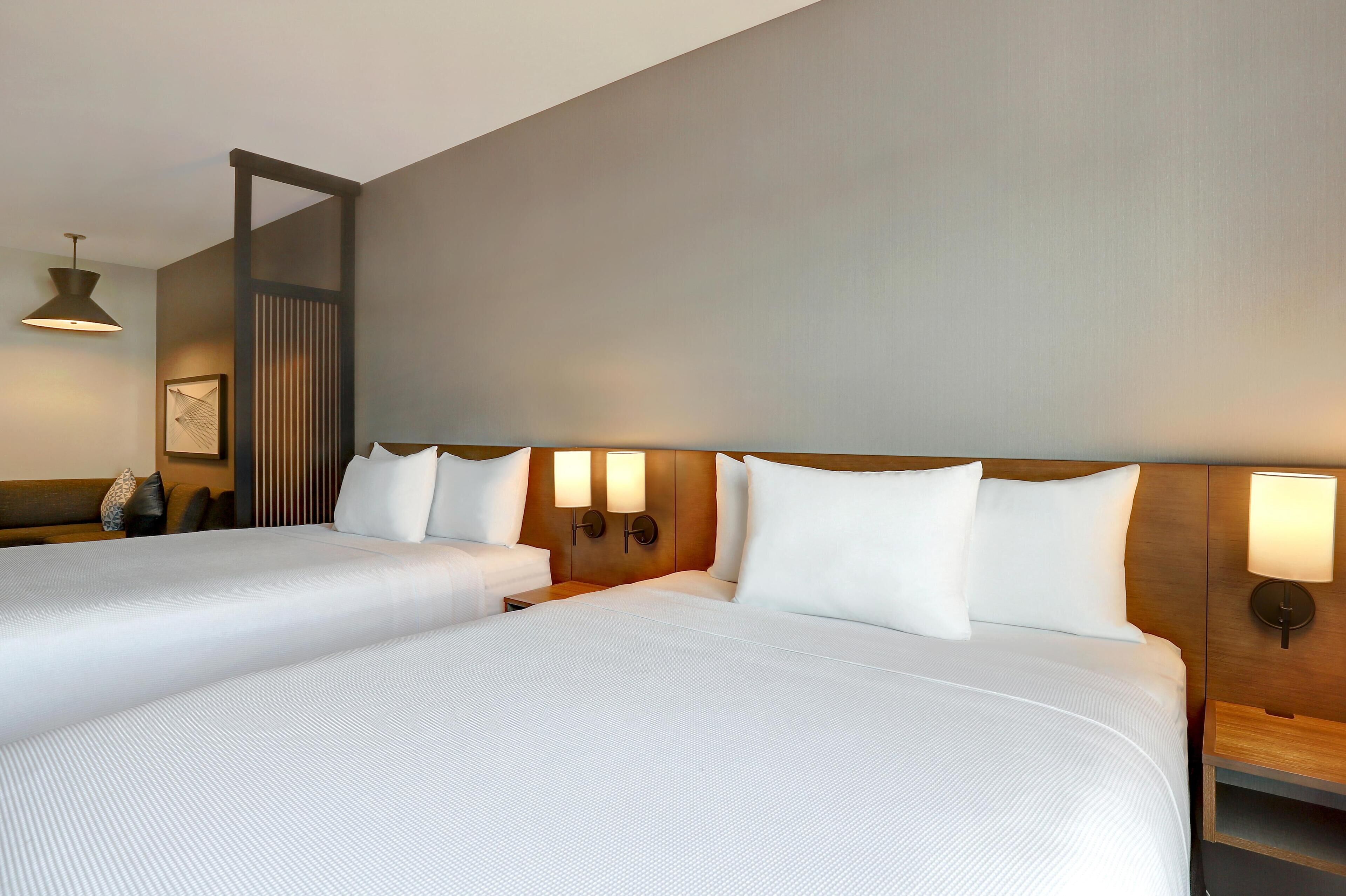A hotel room with two beds, a wooden headboard, bedside lamps, a nightstand, and a hanging light fixture.