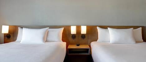 Habitación de hotel con dos camas, cabecero de madera, lámparas de noche y mesitas auxiliares.