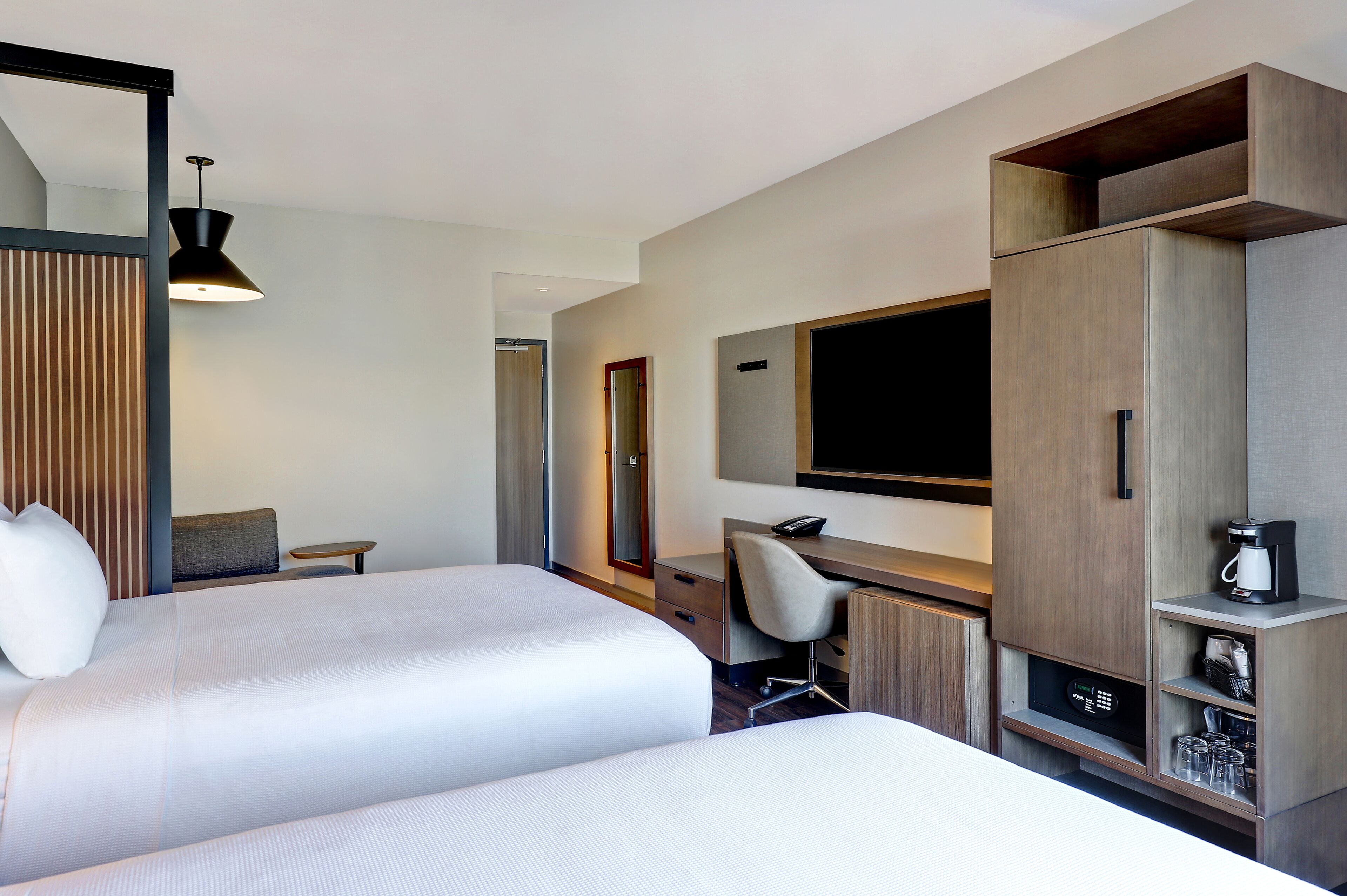 Ein Hotelzimmer mit zwei Betten, einem Schreibtisch, einem Sessel, einem Fernseher und einer Minibar.