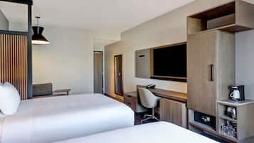 Ein Hotelzimmer mit zwei Betten, einem Schreibtisch, einem Sessel, einem Fernseher und einer Minibar.