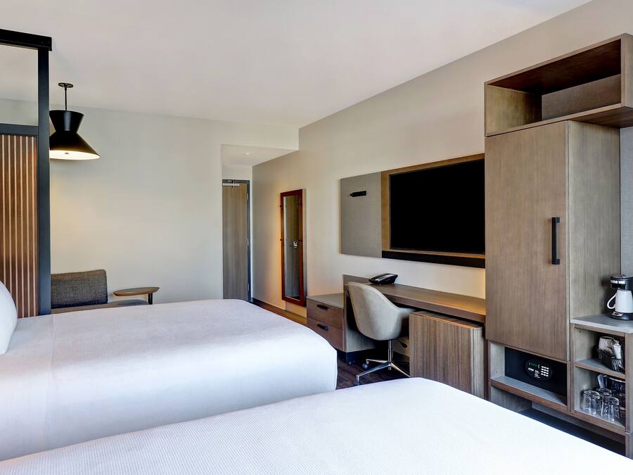 Ein Hotelzimmer mit zwei Betten, einem Schreibtisch, einem Sessel, einem Fernseher und einer Minibar.