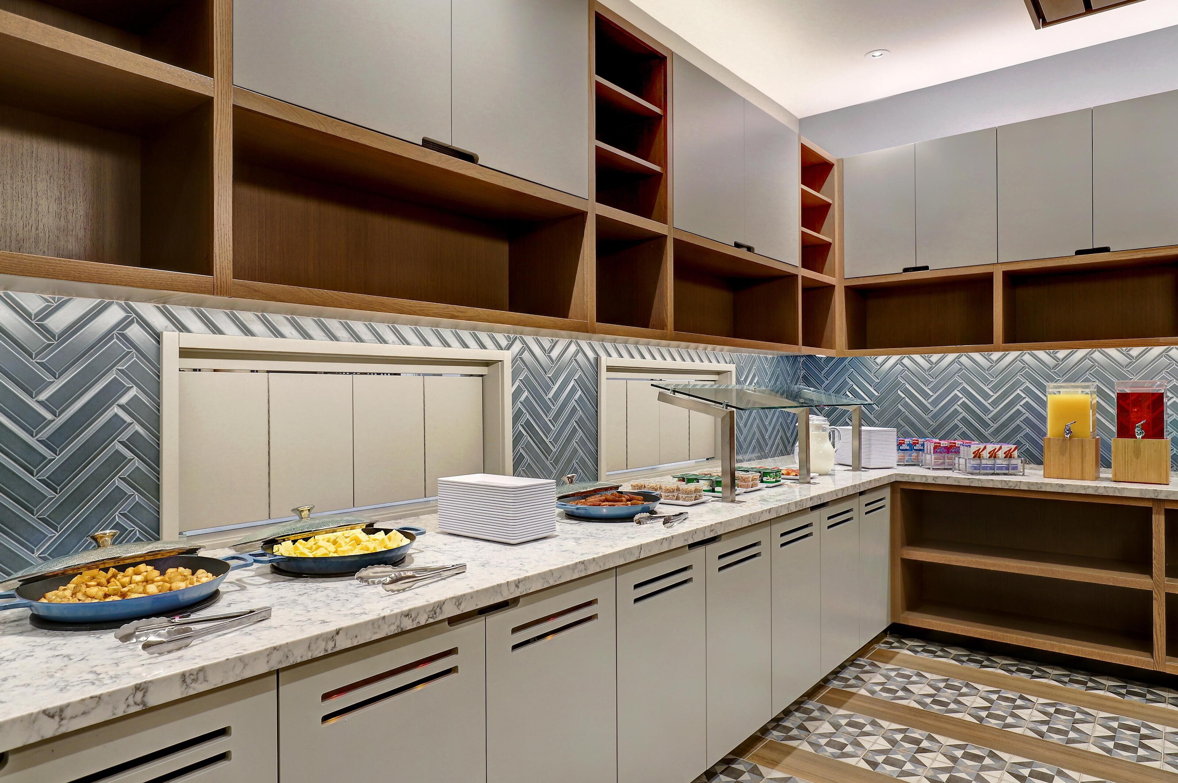 Une cuisine moderne avec des plans de travail en marbre, des armoires en bois et un dosseret orné d’un motif en chevrons.