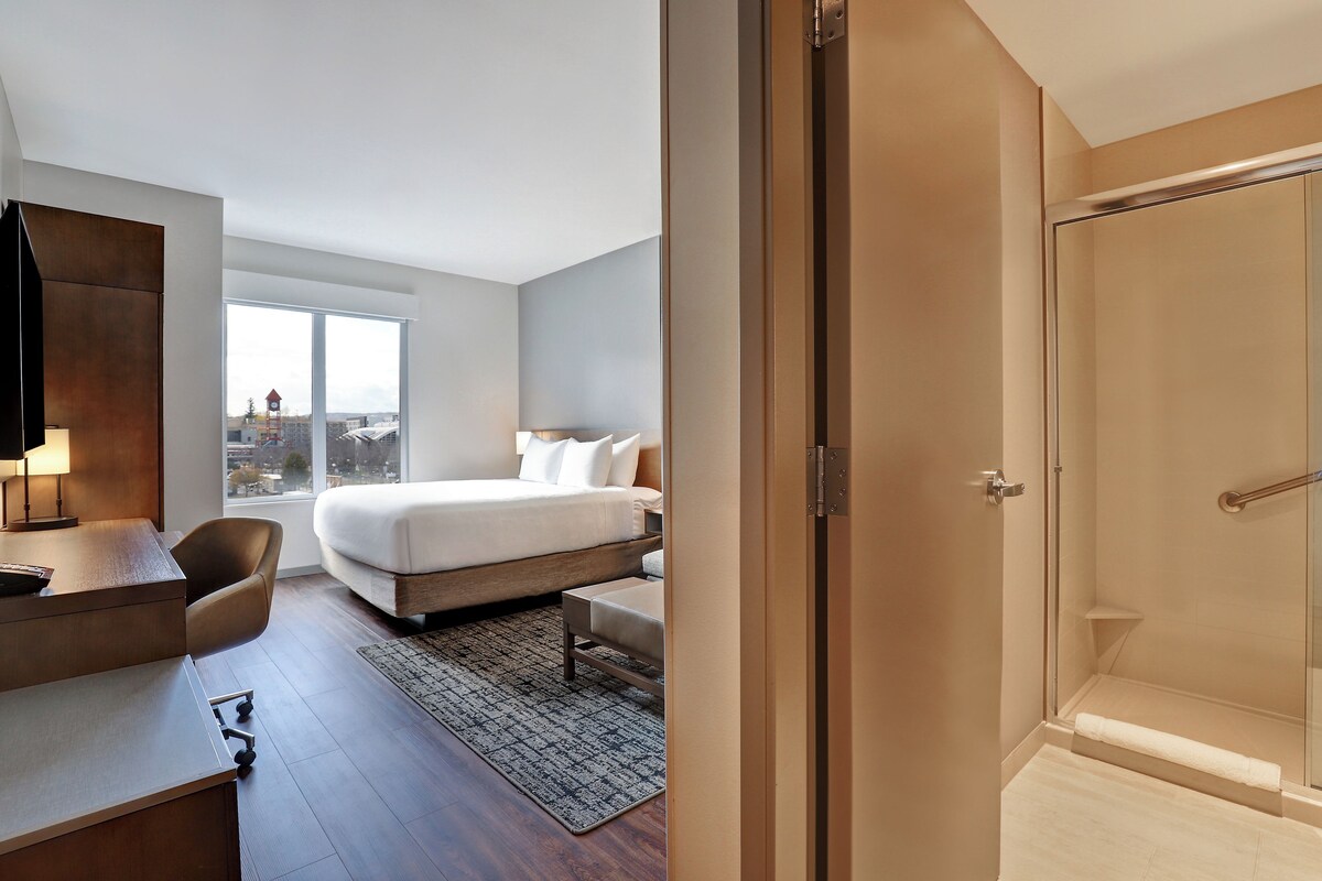 Une chambre d’hôtel moderne équipée d’un lit, d’un bureau, d’une chaise et offrant une vue sur la ville.