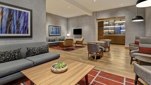 A modern hotel lobby with a grey sofa, a wooden coffee table, and a TV mounted on the wall. - Hyatt Place Prince George (Prince George)