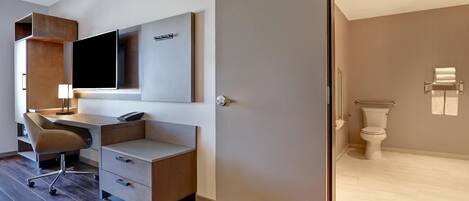 Ein modernes Schlafzimmer mit einem großen Bett, einem Schreibtisch mit Stuhl, einem Flachbildfernseher und einem Badezimmer mit Toilette und Handtuchhalter.