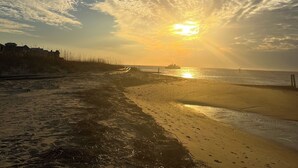 Una spiaggia con un tramonto, nuvole e una costa in lontananza.