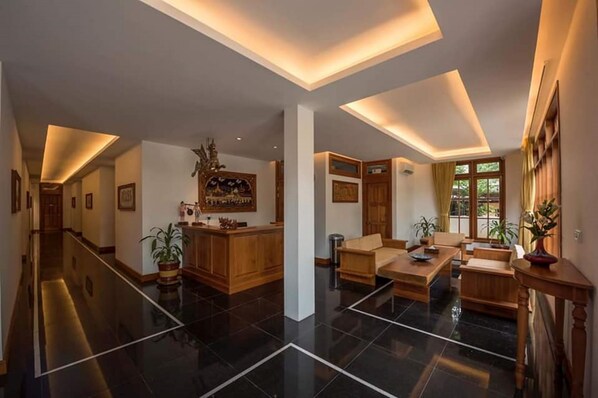 Um hall amplo com balcão de recepção, área de estar e uma grande janela com cortinas.
