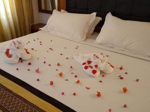 Cama arrumada com lençóis brancos, decorada com pétalas de rosa e almofadas em formato de cisne.