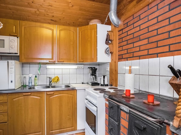A kitchen with wooden cabinets, a white stove, a microwave, and a brick wall.
