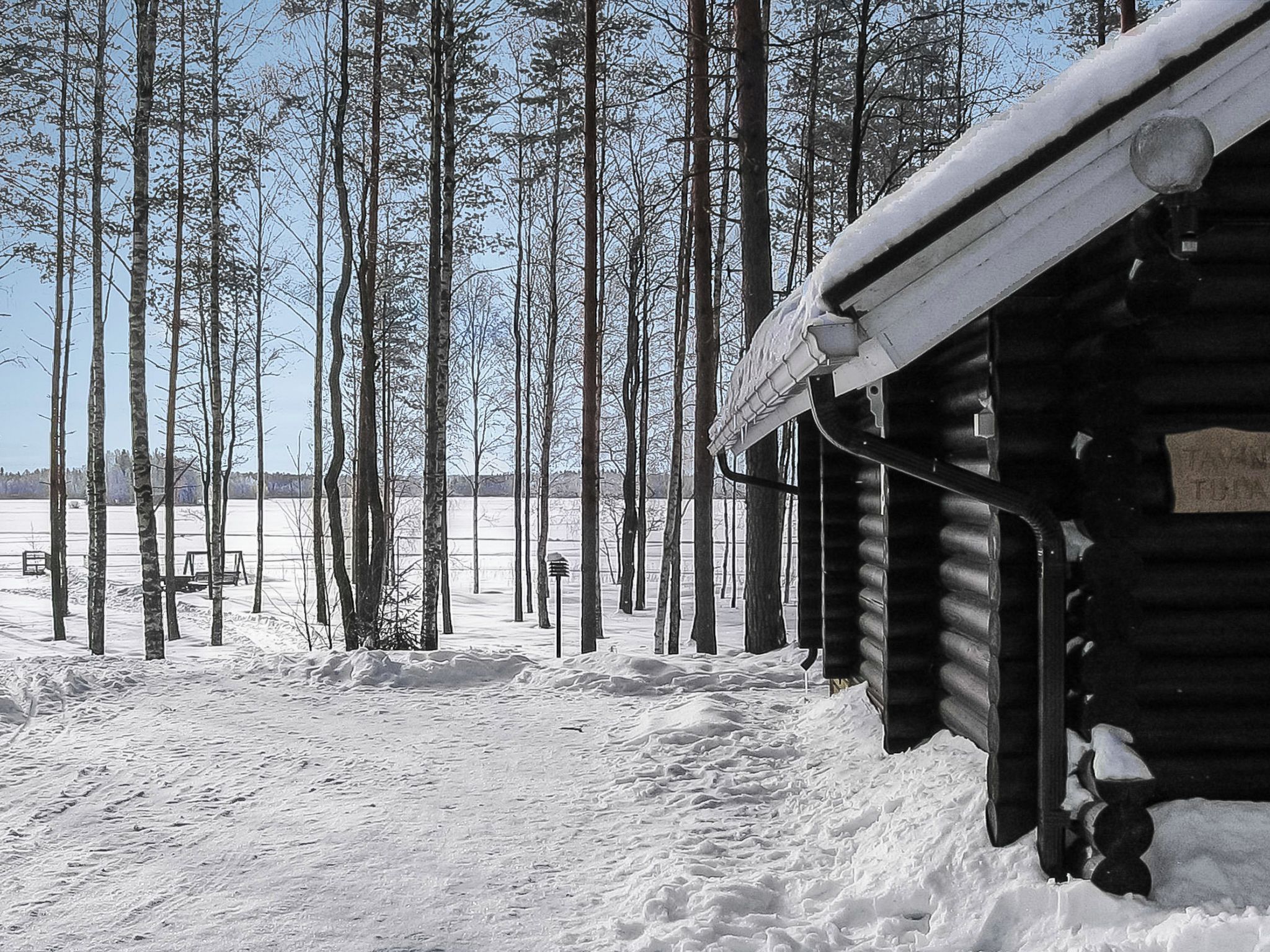 A log cabin with a snow-covered roof, surrounded by a forest of tall, leafless trees.