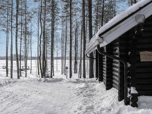 A log cabin with a snow-covered roof, surrounded by a forest of tall, leafless trees. - Tavintupa by Interhome (Pertunmaa)