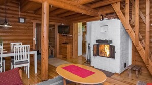 A log cabin interior with a wooden dining table, chairs, a red rug, a fireplace, and a television. - Tavintupa by Interhome (Pertunmaa)