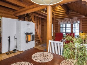 A log cabin interior with a fireplace, wooden beams, a staircase, and a dining area with a table and chairs. - Tavintupa by Interhome (Pertunmaa)