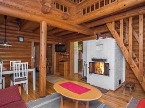 A cozy cabin interior with a wooden ceiling, a fireplace, a dining area with white chairs, and a television mounted on the wall. - Tavintupa by Interhome (Pertunmaa)