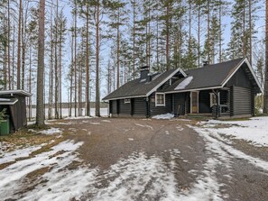 A log cabin with a gravel driveway and a snow-covered ground, surrounded by tall trees. - Tavintupa by Interhome (Pertunmaa)