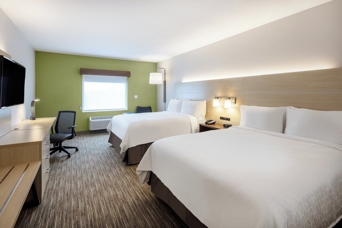 Quarto de hotel com duas camas, uma escrivaninha, uma cadeira, uma televisão e uma janela com persianas.