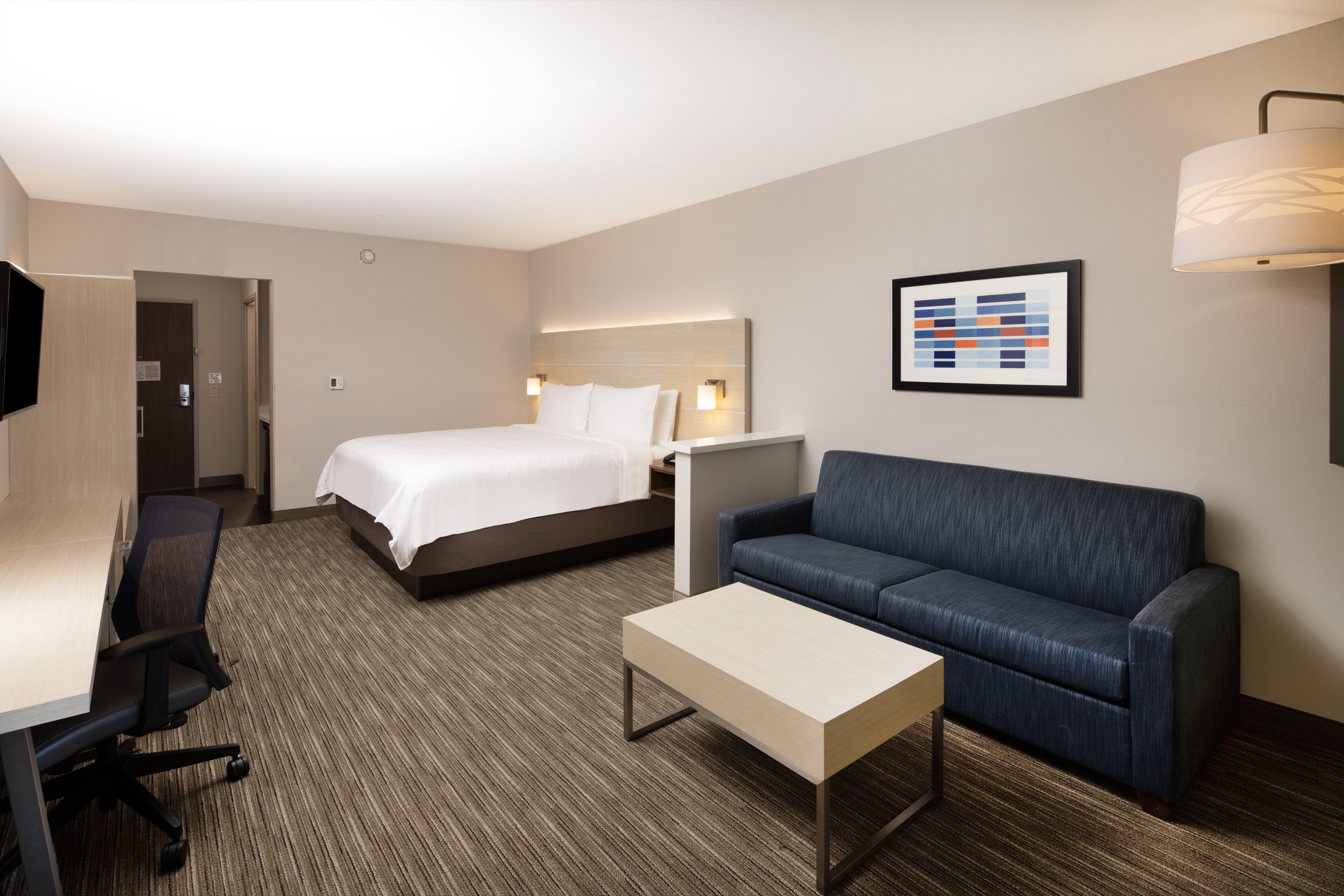 A hotel room with a bed, a sofa, a desk, and a TV.