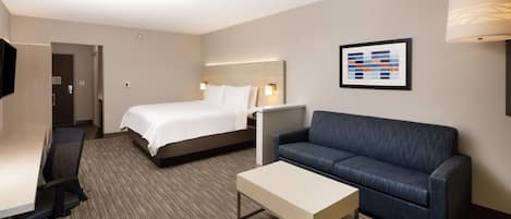 A hotel room with a bed, a sofa, a desk, and a TV.