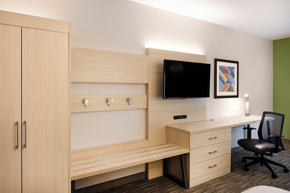 Quarto de hotel com uma escrivaninha de madeira, uma cadeira de escritório preta, uma televisão de tela plana e um quadro pendurado na parede.