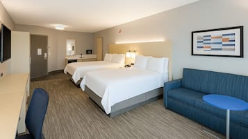 A hotel room with two beds, a desk, a chair, a blue sofa, and a small table.