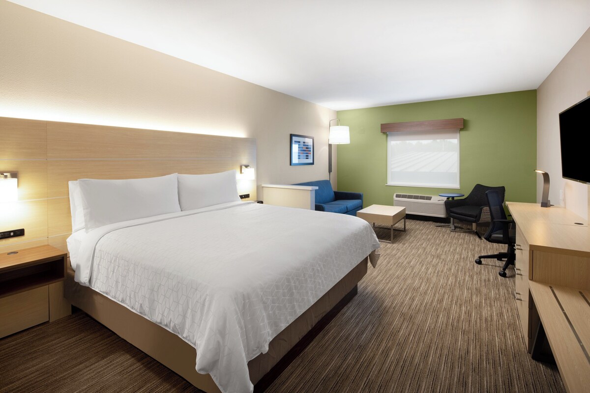 Quarto de hotel com uma cama grande, uma escrivaninha, uma cadeira e uma televisão.