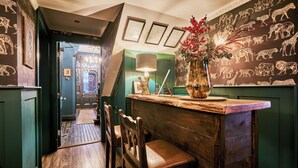 A wooden bar area with a green wall, a vase with red flowers, and framed animal illustrations on the wall.