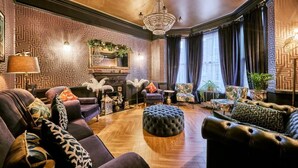 A luxurious living room with patterned wallpaper, a chandelier, leather sofas, and a fireplace.