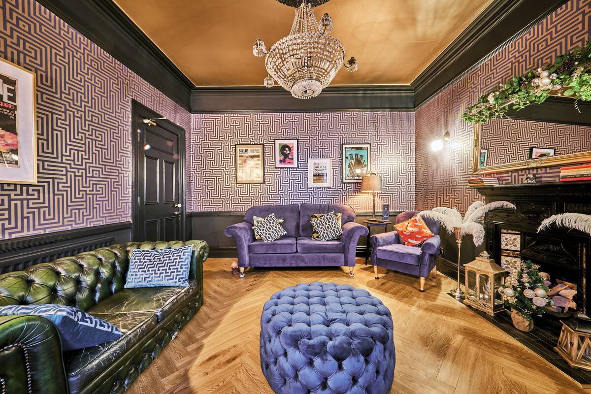 Ein Zimmer mit strukturierten Tapeten, einer Kristallleuchter, einem Kamin und Ledermöbeln.