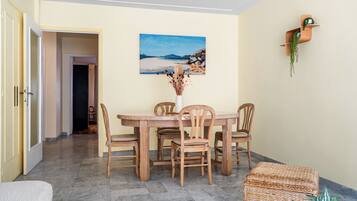 Un coin repas avec une table ronde en bois et des chaises, un tableau accroché au mur et une petite étagère avec une plante.
