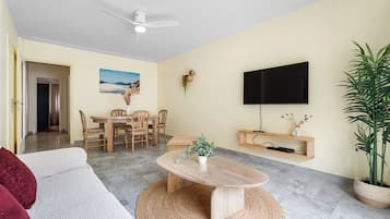 Un salon comprenant un canapé, une table basse, un téléviseur et un coin repas avec des chaises et une table.