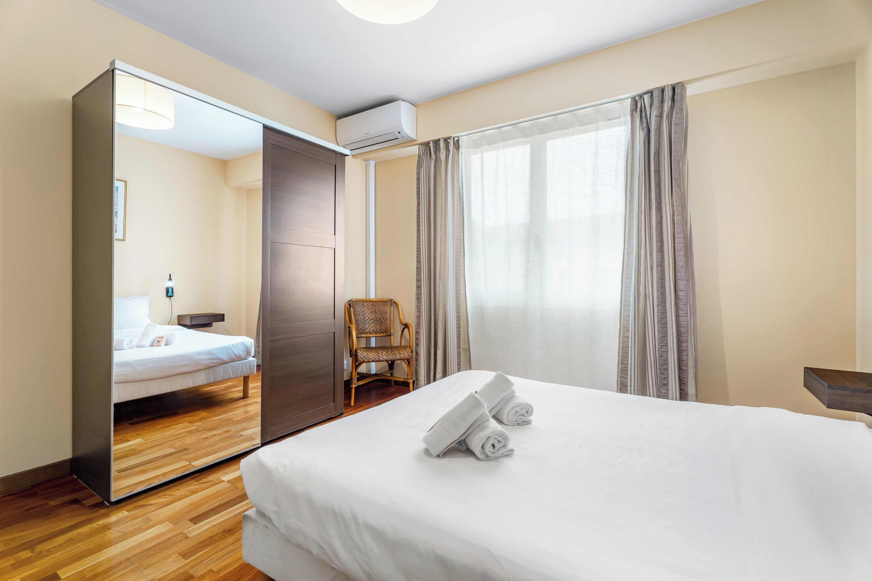 A hotel room with a bed, a chair, a mirror, and a window with curtains.