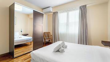 A hotel room with a bed, a chair, a mirror, and a window with curtains.