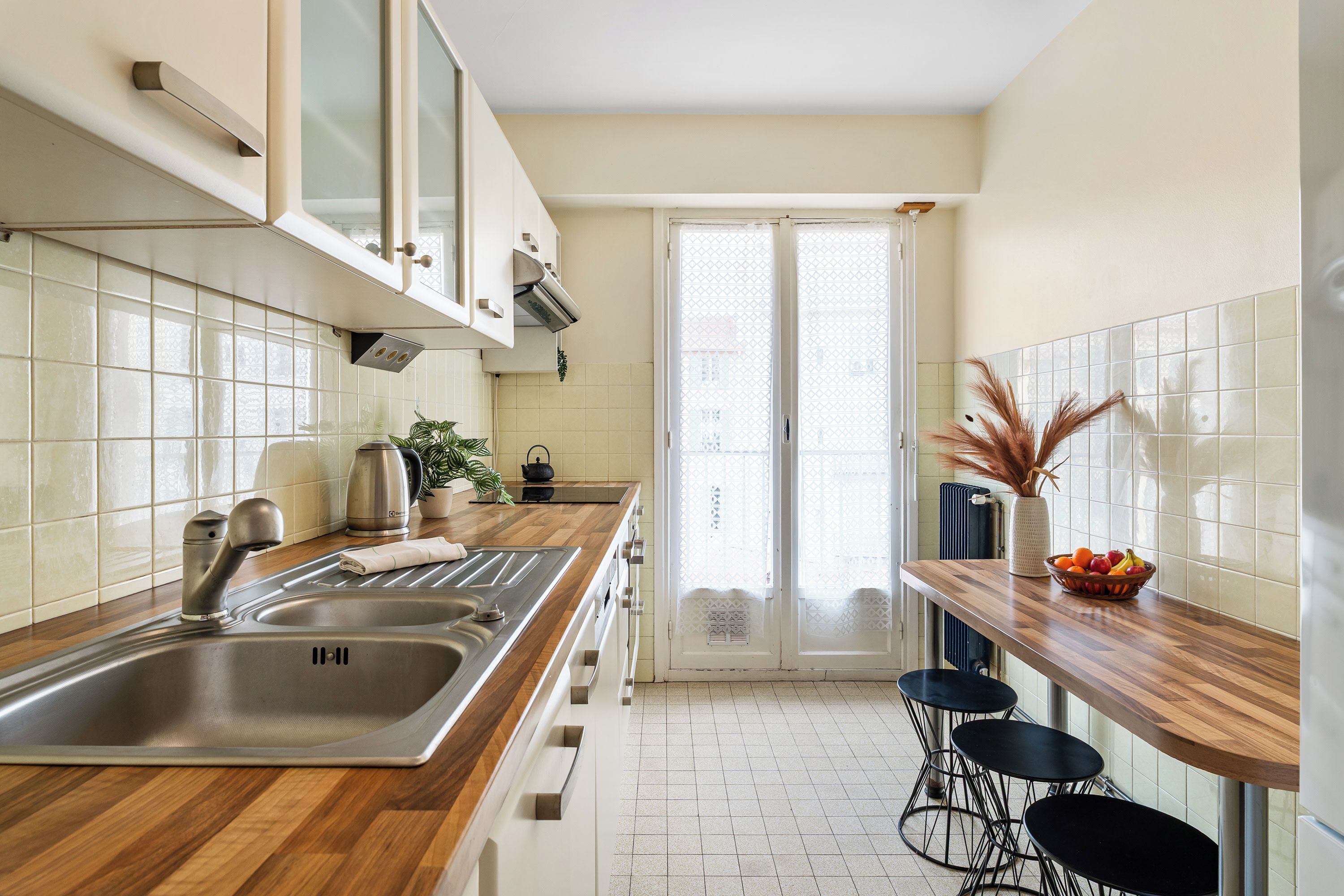 Une cuisine moderne dotée d’un plan de travail en bois, d’un évier en acier inoxydable et offrant une vue sur l’extérieur.