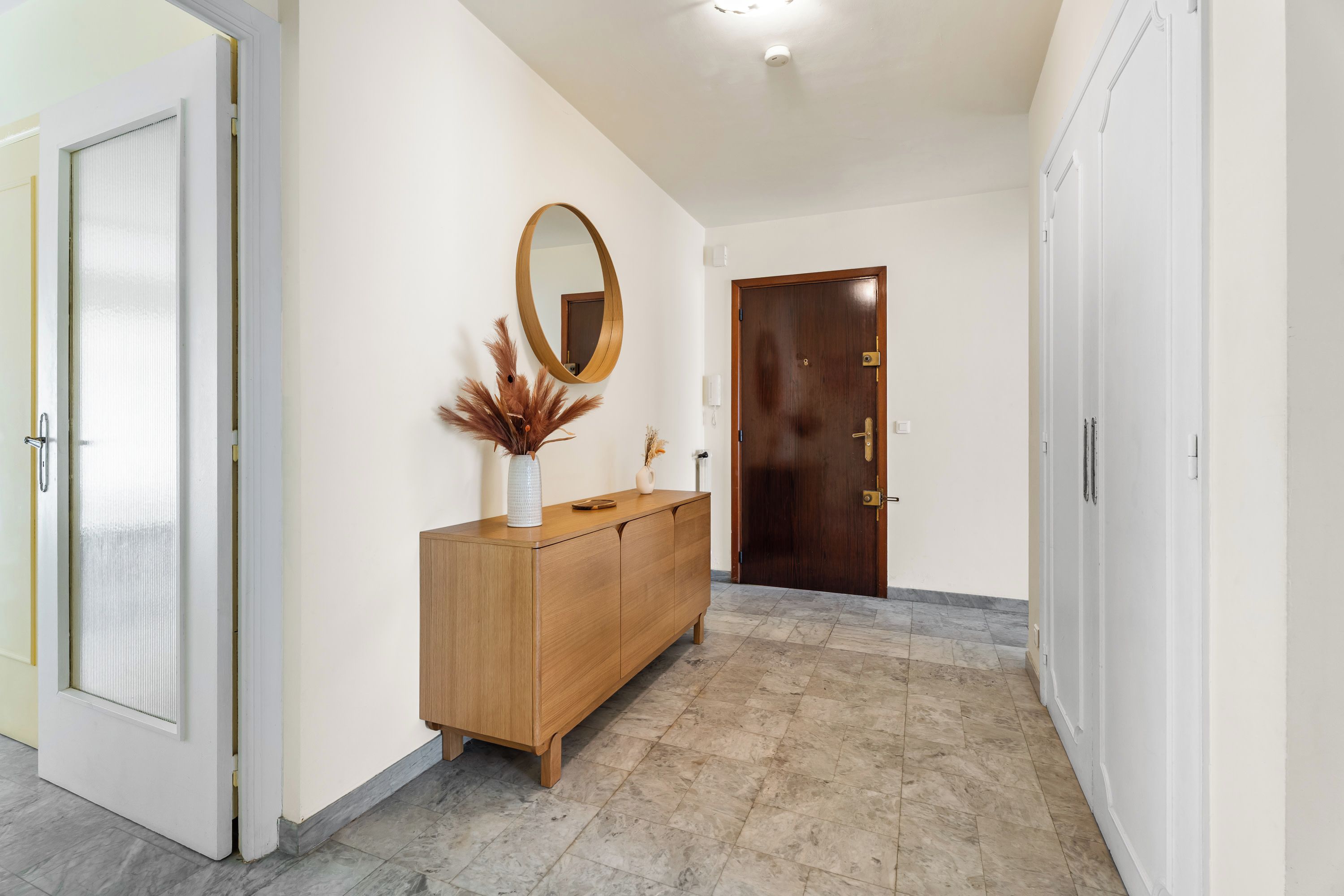 Un couloir avec une armoire en bois, un miroir et une porte.