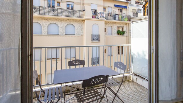 Een balkon met een tafel en stoelen, met uitzicht op een rij gebouwen met balkons.