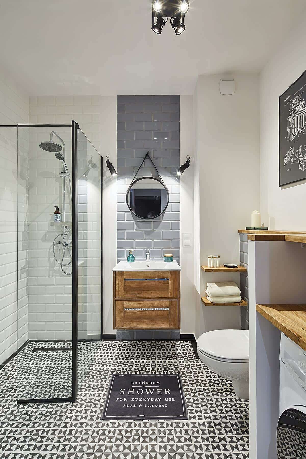 A modern bathroom with a glass shower enclosure, a wooden vanity, a white toilet, and a patterned floor.