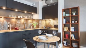 A modern kitchen with dark cabinets, a wooden countertop, and a dining area with a round table and chairs. - Elegant Apartment in Zoliborz | Balcony and Parking (Warszawa)