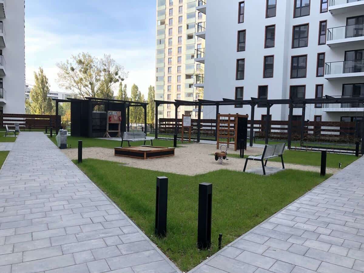 Sisäpiha, jossa on puinen leikkiväline, penkkejä ja pieni puutarha-alue.