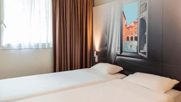 Une chambre d’hôtel avec un lit, une fenêtre avec des rideaux et une vue sur un bâtiment à l’extérieur.
