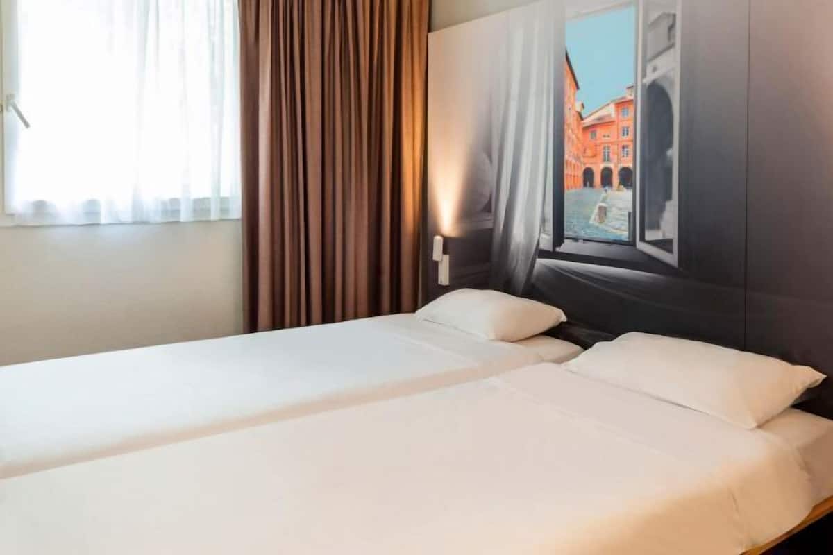 Une chambre d’hôtel avec un lit, une fenêtre avec des rideaux et une vue sur un bâtiment à l’extérieur.