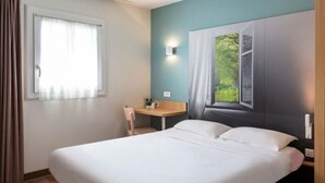 Une chambre d’hôtel équipée d’un lit, d’un bureau, d’une chaise, d’une fenêtre avec des rideaux et d’une lampe fixée au mur.