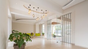 A spacious lobby with a modern design, featuring a large potted plant, a seating area with green chairs, and a glass partition. - Kiluwa Apartments & Spa  by Dunhill Serviced Apartments (Nairobi)