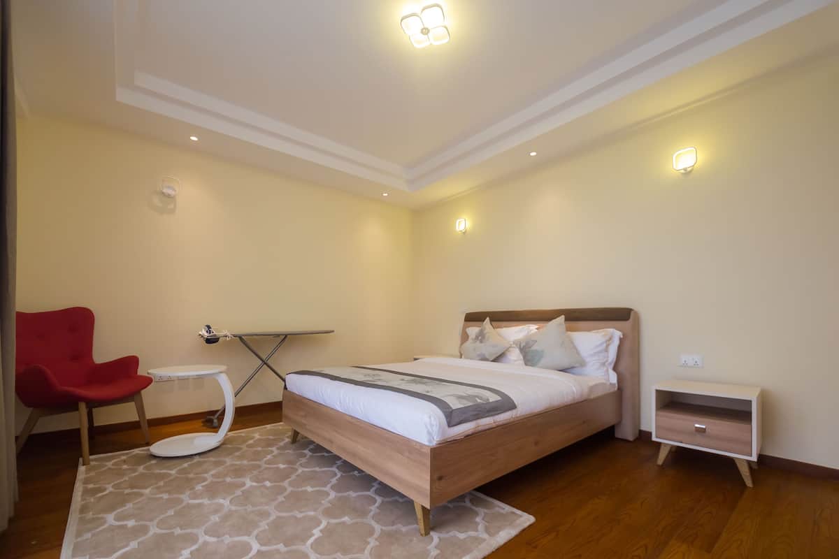 A bedroom with a bed, bedside table, nightstand, red chair, and a small table.