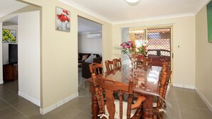 Un comedor con una mesa de vidrio rodeada de sillas de madera, un jarrón con flores y un cuadro en la pared.